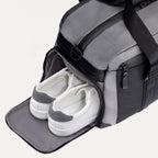  Travelpro Altitude Day-to-Day Duffel in Falcon Grey, with shoe compartment open and sneakers neatly stowed inside.
