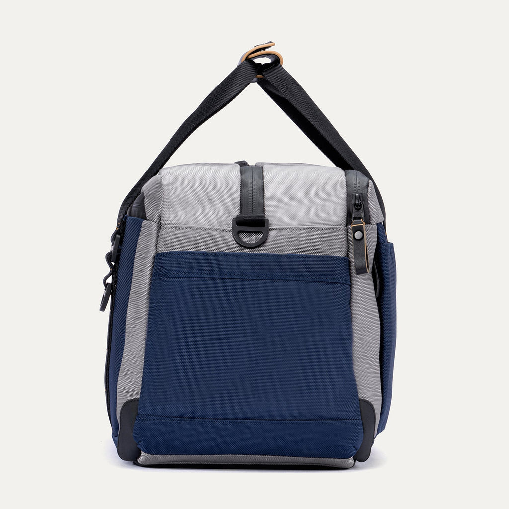 Side view of the Travelpro Altitude Day-to-Day Duffel in Stellar Navy/Grey, featuring an adjustable shoulder strap and side zip pocket.
