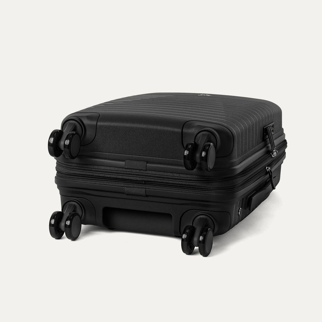 Side-profile view of the Optima Expandable Compact Carry-on Spinner in Black, highlighting the base construction and the self-aligning MagnaTrac® spinner wheels that ensure smooth, drift-free mobility.