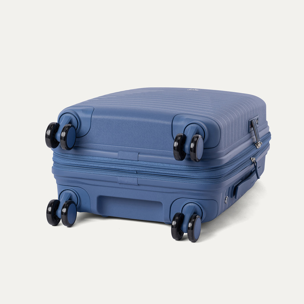 Side-profile view of the Optima Expandable Compact Carry-on Spinner in Horizon Blue, highlighting the base construction and the self-aligning MagnaTrac spinner wheels that ensure smooth, drift-free mobility.