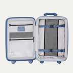 Open interior view of the Horizon Blue Optima Expandable Carry-on Spinner, showing the main packing compartment with a zippered mesh-paneled divider on the left and a removable multi-pocket organizer panel secured with compression straps on the right against a clean off-white background.