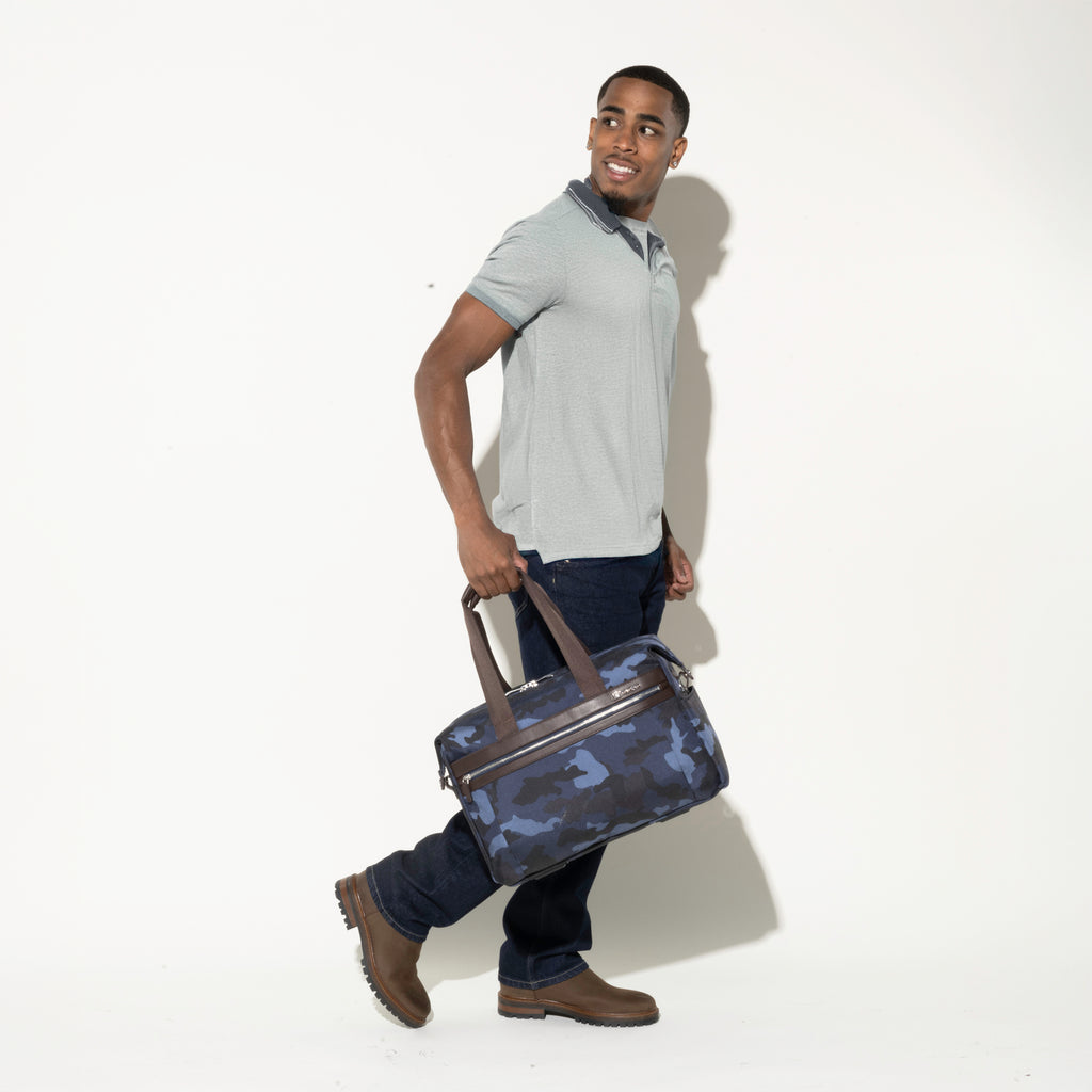 Person carrying the Travelpro Platinum Elite Underseat Tote in camouflage by the top handles, showcasing compact, on-the-go convenience.
