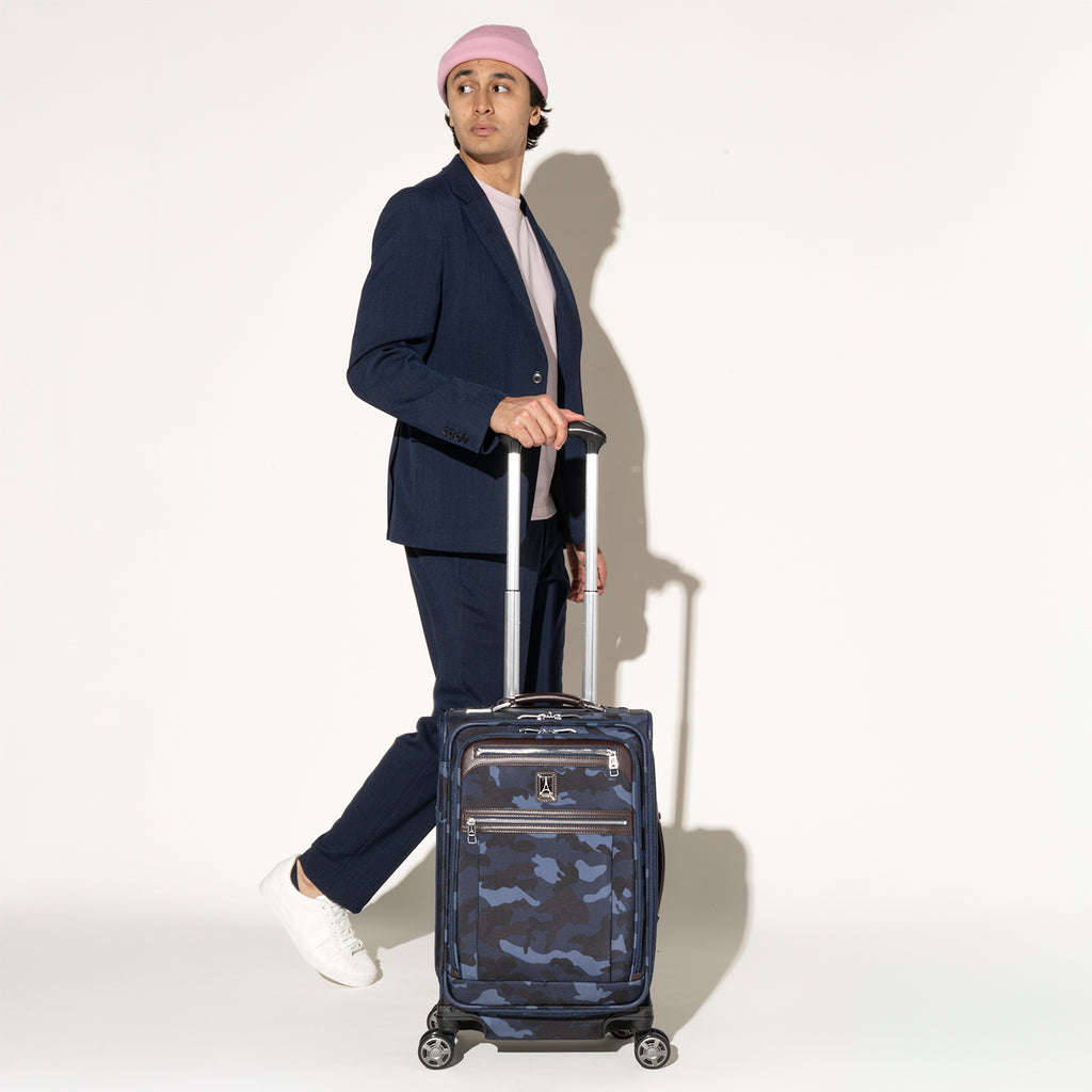 Person walking while rolling a Travelpro Platinum Elite Carry-On Spinner in camouflage using the extended PowerScope Extension Handle.
