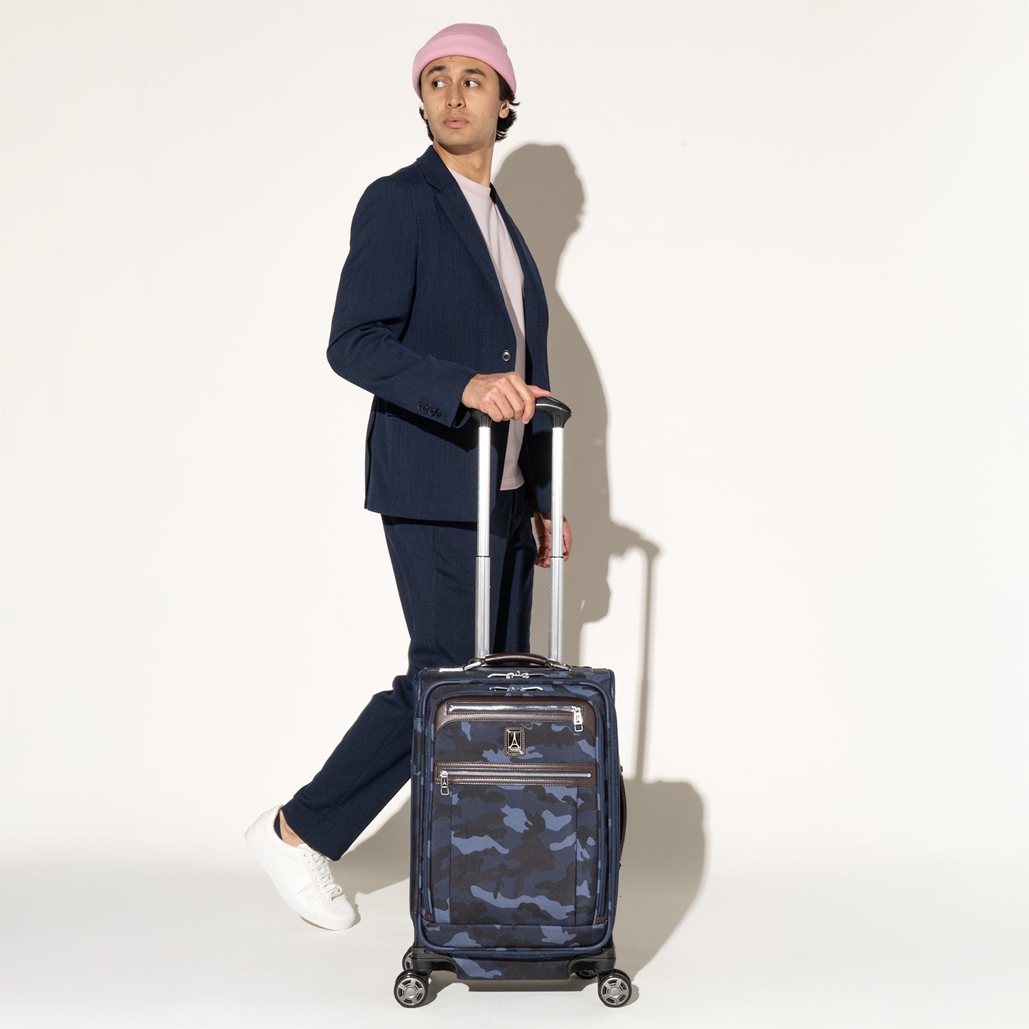 Person walking while rolling a Travelpro Platinum Elite Carry-On Spinner in camouflage using the extended PowerScope Extension Handle.
