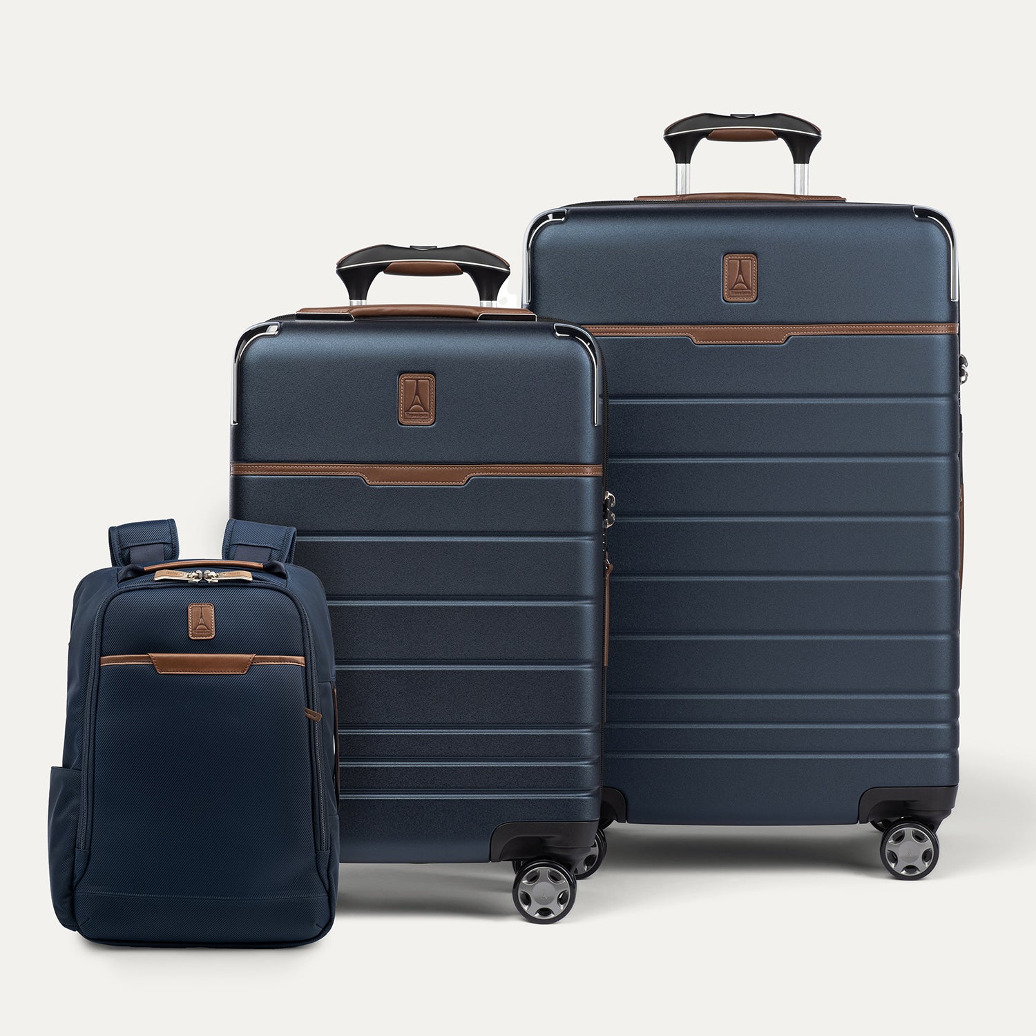 front group view of the travelpro x travel plus leisure three-piece luggage set in monaco blue, featuring a slim backpack standing on the left, a carry-on spinner suitcase in the center, and a medium check-in spinner suitcase standing behind them on the right, all showcasing rich blue polycarbonate or fabric exteriors with elegant brown leather trim and extended telescoping handles.