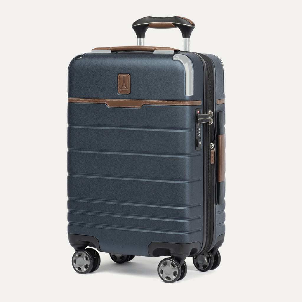 front three-quarter view of the monaco blue travelpro x travel plus leisure carry-on spinner suitcase standing upright, showcasing its sleek hardshell finish, premium brown leather trim on the top and side, four 360-degree self-aligning wheels, and extended telescoping handle with a matching brown leather grip.