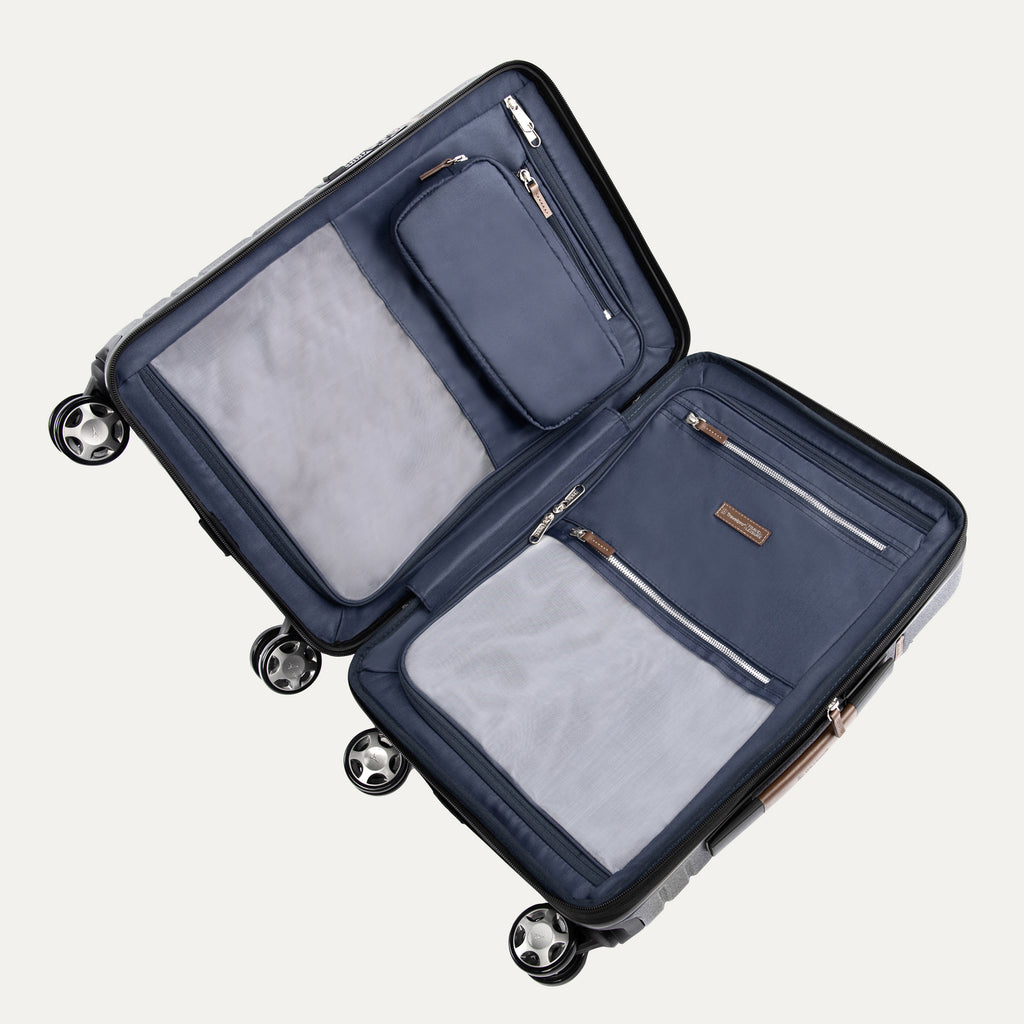interior view of the open monaco blue travelpro x travel plus leisure hardshell spinner suitcase lying flat, showcasing its fully lined navy blue compartments, zippered privacy separator panels with built-in mesh and solid organizing pockets, and elegant brown leather zipper pulls.