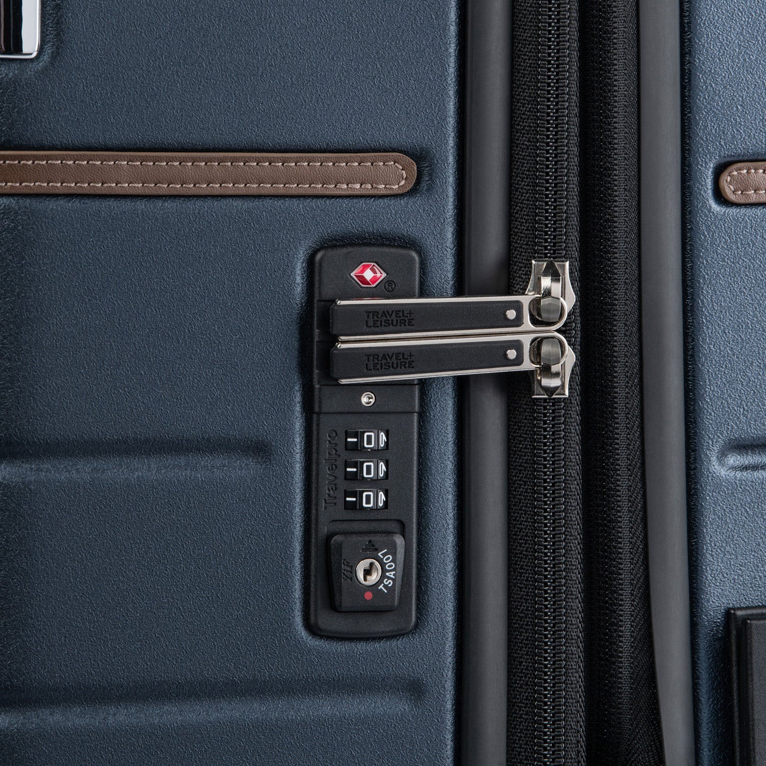 close-up detail view of the monaco blue travelpro x travel plus leisure suitcase, highlighting the integrated recessed TSA-approved combination lock with premium silver metal zipper pulls and elegant brown leather trim detailing against the durable textured hardshell exterior.
