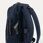 close-up side view of the monaco blue travelpro x travel plus leisure slim backpack, highlighting a zippered side storage pocket with an elegant brown leather trim accent, featuring a small personal item stored inside and durable navy blue fabric construction.