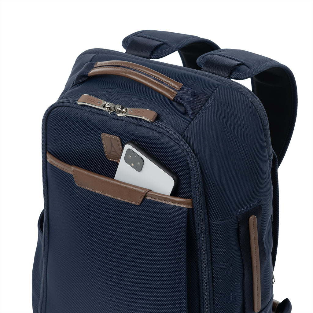 close-up front view of the monaco blue travelpro x travel plus leisure slim backpack, highlighting a convenient top-loading zippered quick-access pocket featuring elegant brown leather trim with a smartphone partially tucked inside, showcasing the durable textured blue fabric construction.