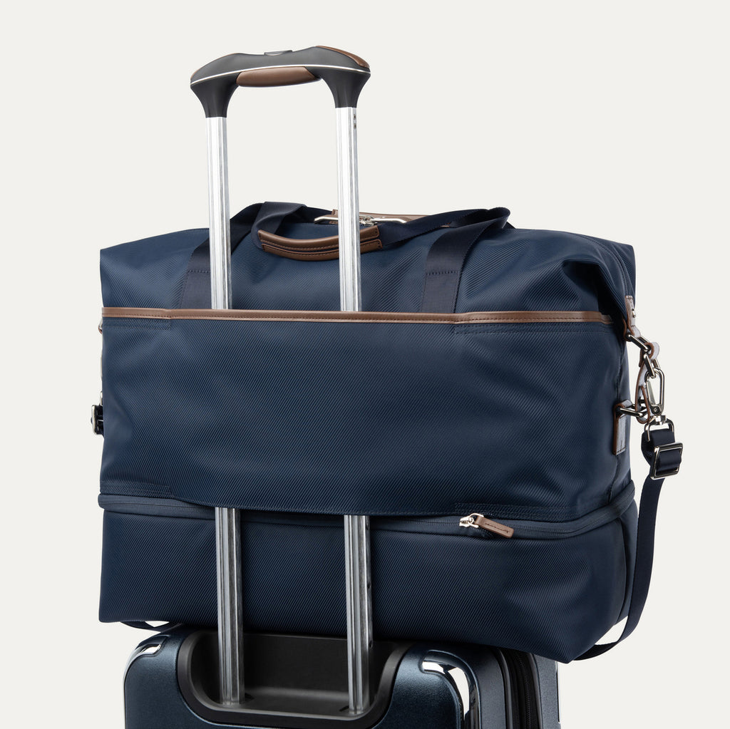 Blue weekender with rear strap over suitcase handle on a white background