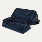 Navy blue weekender with brown straps and open drop bottom compartment on a white background