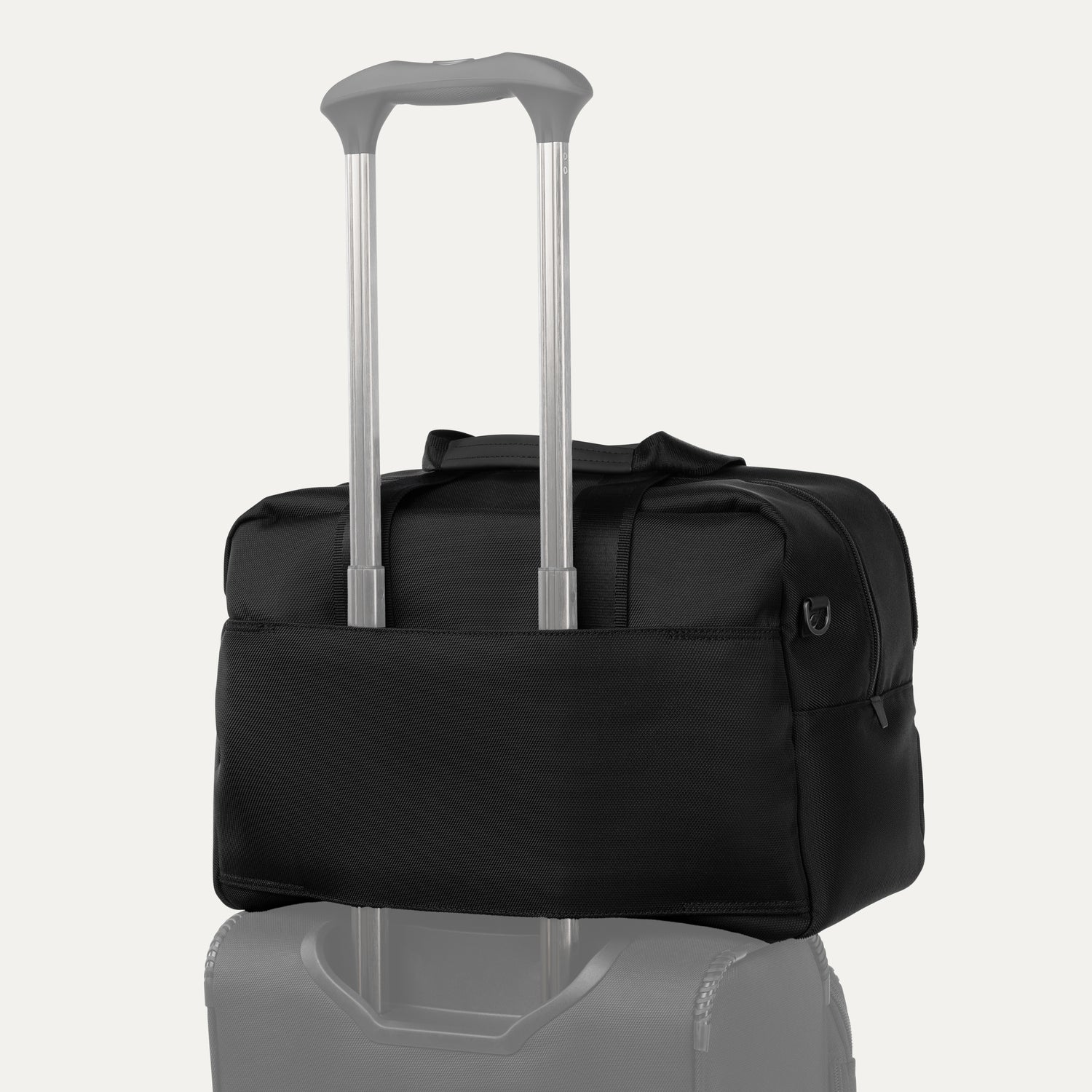 Black tote bag stacked on top of a piece of luggage with a light gray background