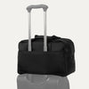 Black tote bag stacked on top of a piece of luggage with a light gray background