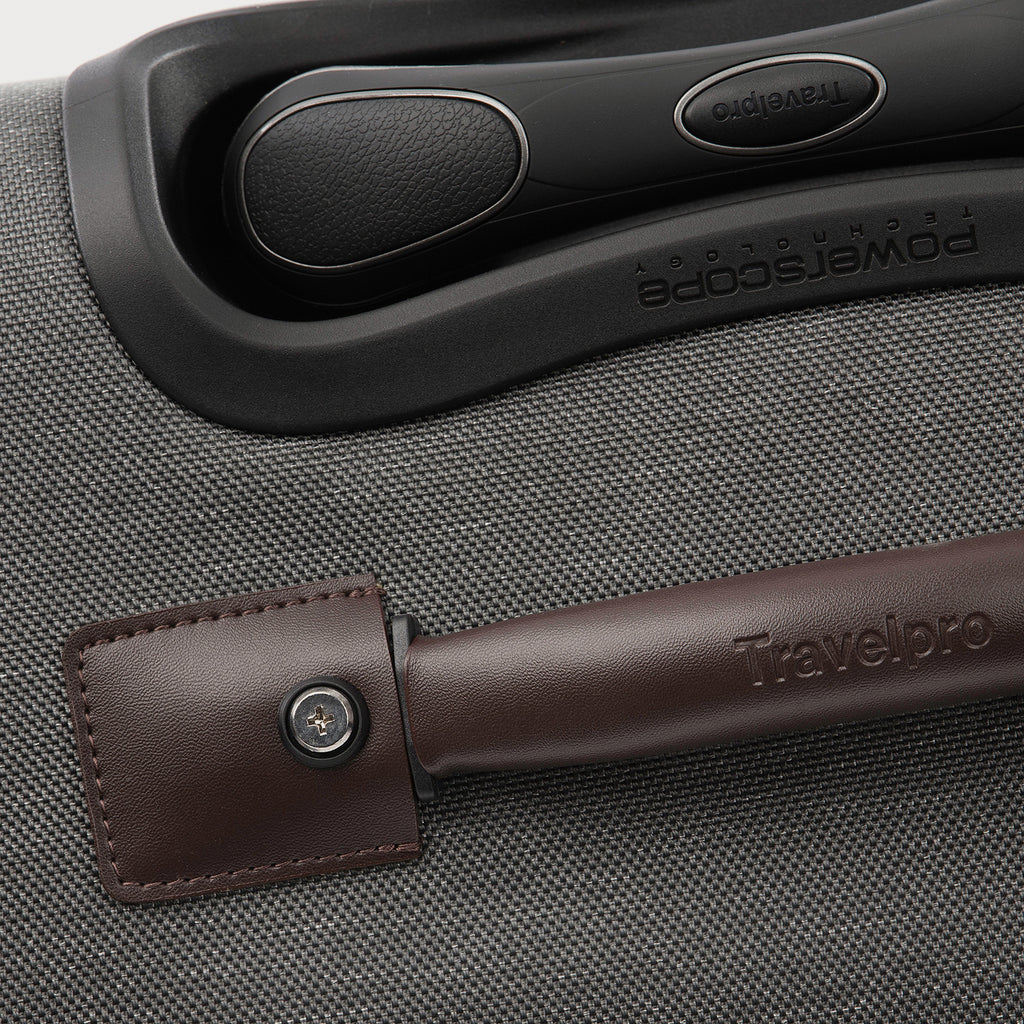 Close-up of a suitcase handle with a brown leather wrap on a gray textured suitcase.