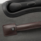 Close-up of a suitcase handle with a brown leather wrap on a gray textured suitcase.