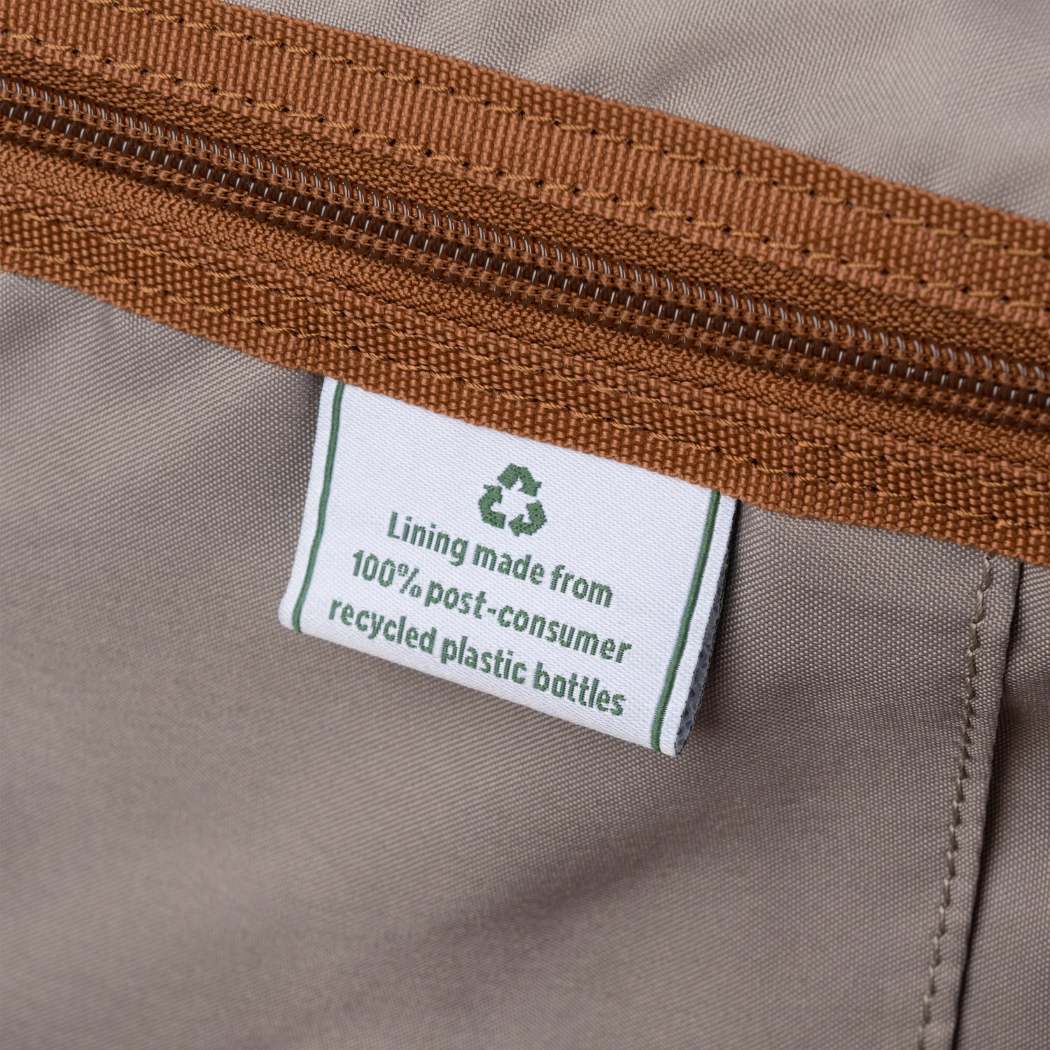 Close-up of a label indicating recycled plastic lining on a product with brown zipper.