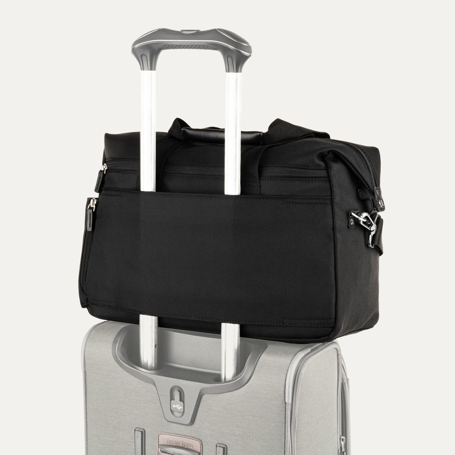 Black tote secured over suitcase handle using rear strap, on a white background