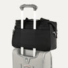 Black tote secured over suitcase handle using rear strap, on a white background