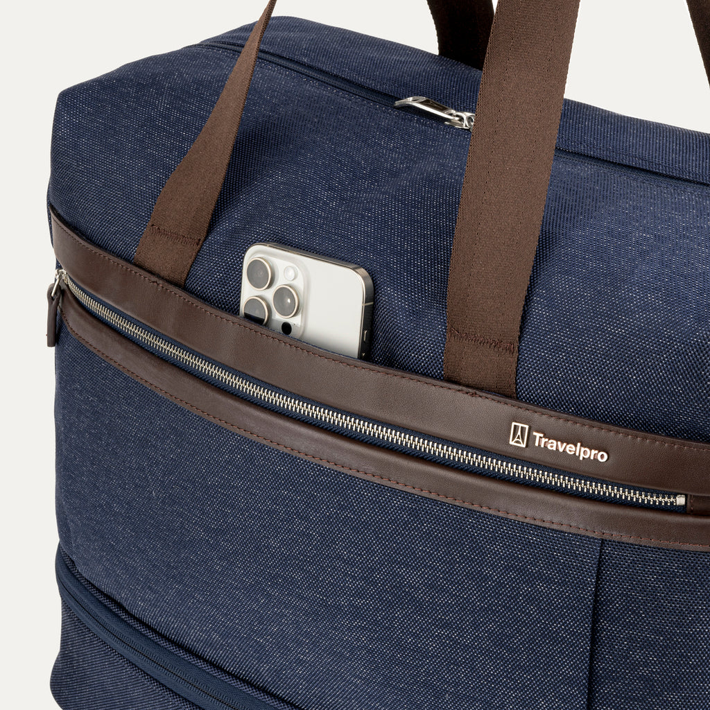 Blue duffel bag with brown straps and a phone in a pocket, featuring the Travelpro logo.