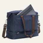 Blue duffel bag with brown straps containing a laptop on a white background