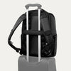 Black backpack with a black strap over suitcase handle on a white background