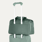 Green rolling suitcase with a tote stacked on top on a white background