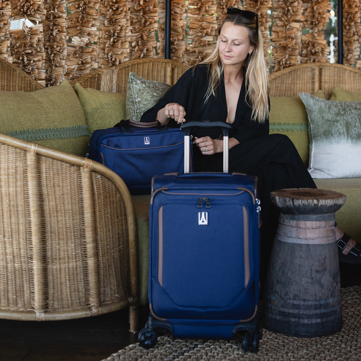 Woman sitting on a couch with two blue suitcases in front of her.