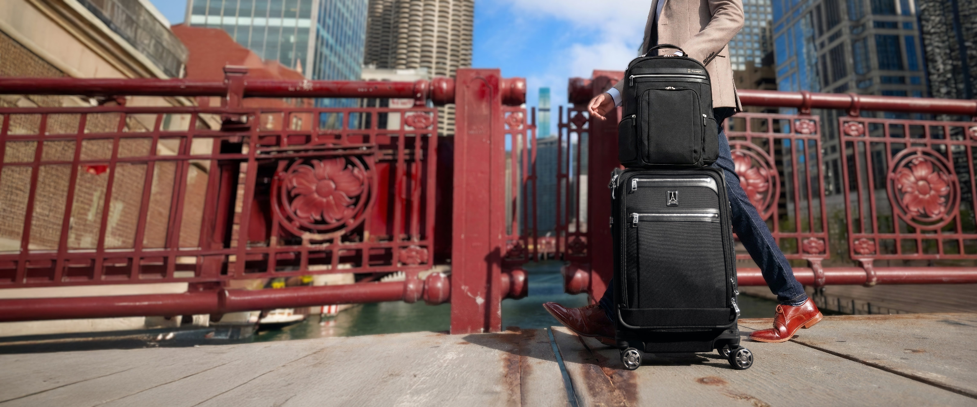 Person with black suitcases on a city street with red metal railing and buildings in the background