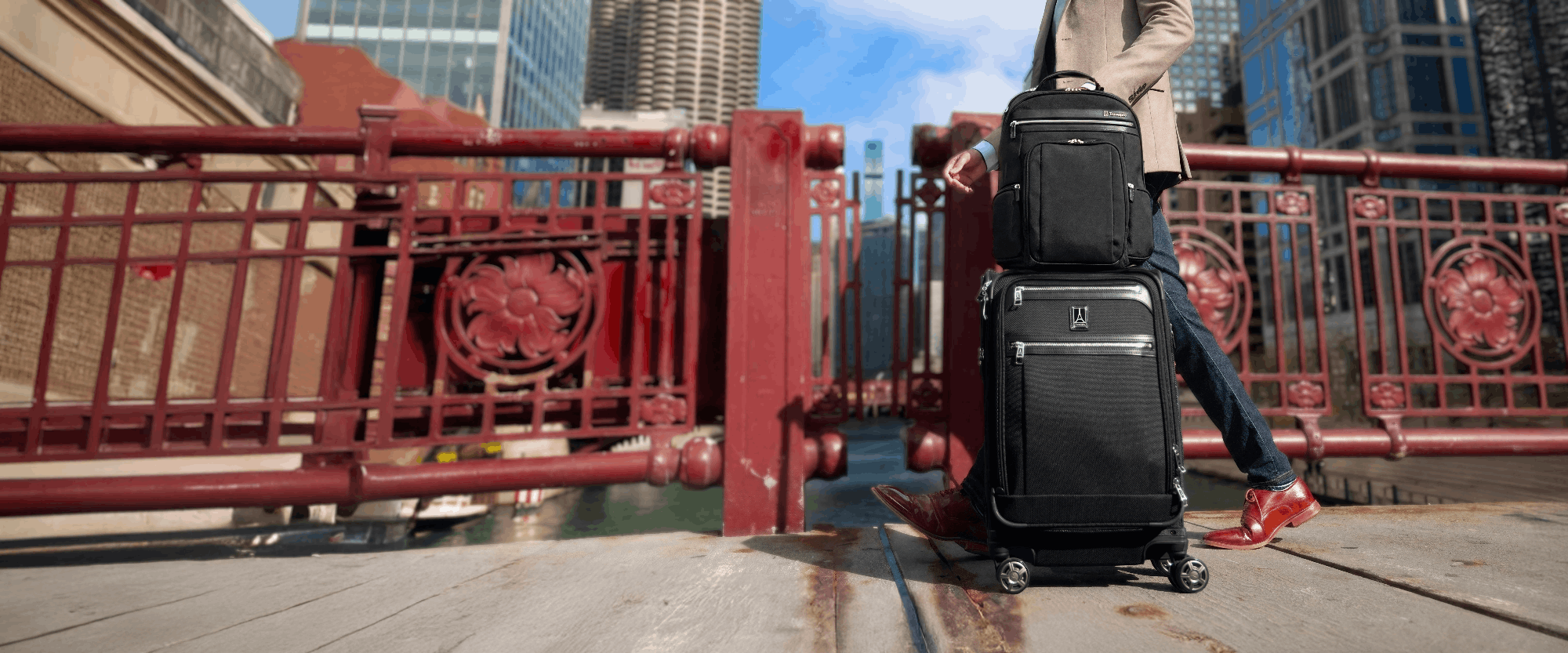 Person with two suitcases on a city street with a red metal railing and buildings in the background.