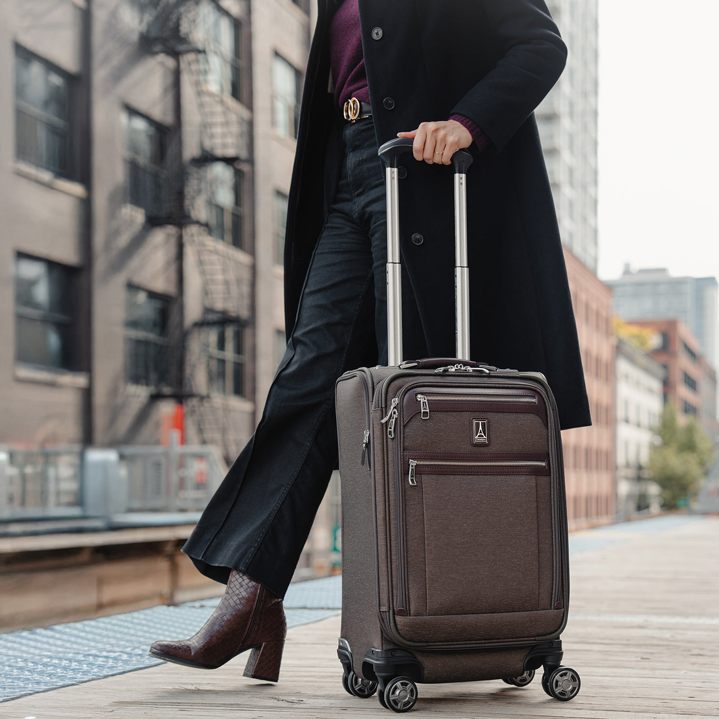 Person in a black coat holding a brown suitcase on a city street.