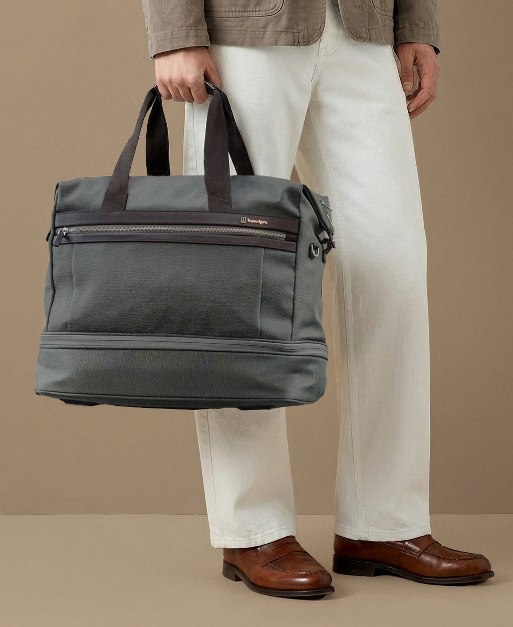 Person holding a gray duffel bag against a beige background