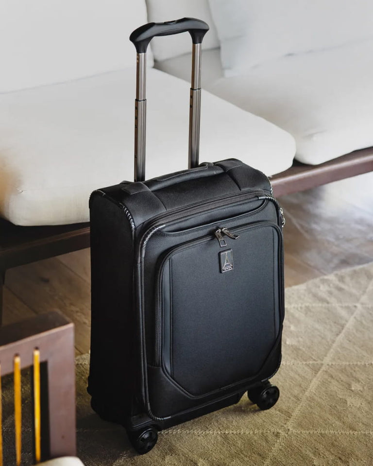 Crew Classic carry-on spinner in black beside a sofa