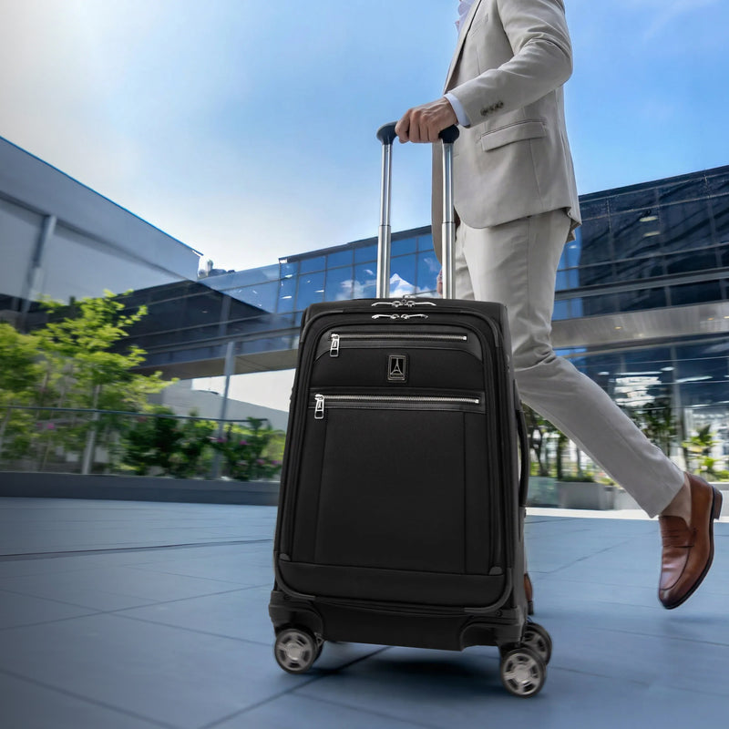 Person in a suit pulling a black suitcase on wheels outdoors.