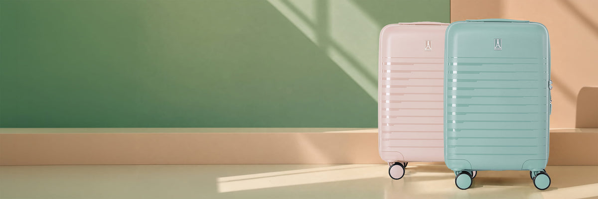 Two hard-shell spinner suitcases standing upright against a minimalist wall. The suitcase on the left is pastel pink, and the suitcase on the right is pastel mint green.