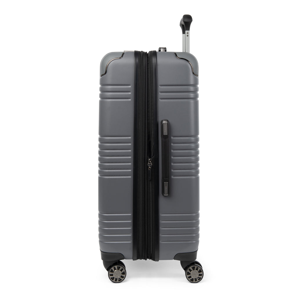 Side profile view of the Travelpro Roundtrip Hardshell Medium Check-In Suitcase in Gunmetal Gray, showing textured hardshell design, expansion zipper open, black telescoping handle, and four spinner wheels against white background.