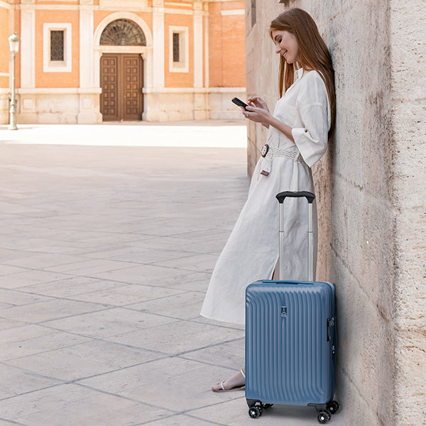 Woman smiling at the phone while vacationing and using a Maxlite Air hard shell carry on suitcase in Blue.