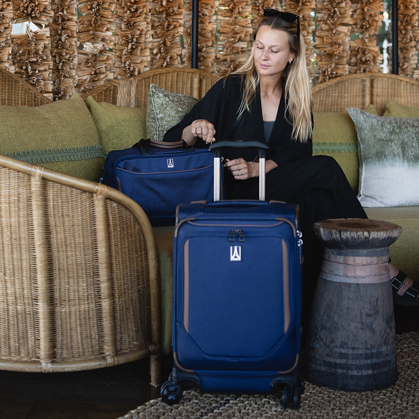 lifestyle shot of a woman with the travelpro® crew™ classic true navy luggage set, featuring the softside expandable carry-on spinner and the matching rolling underseat tote in a lounge setting.