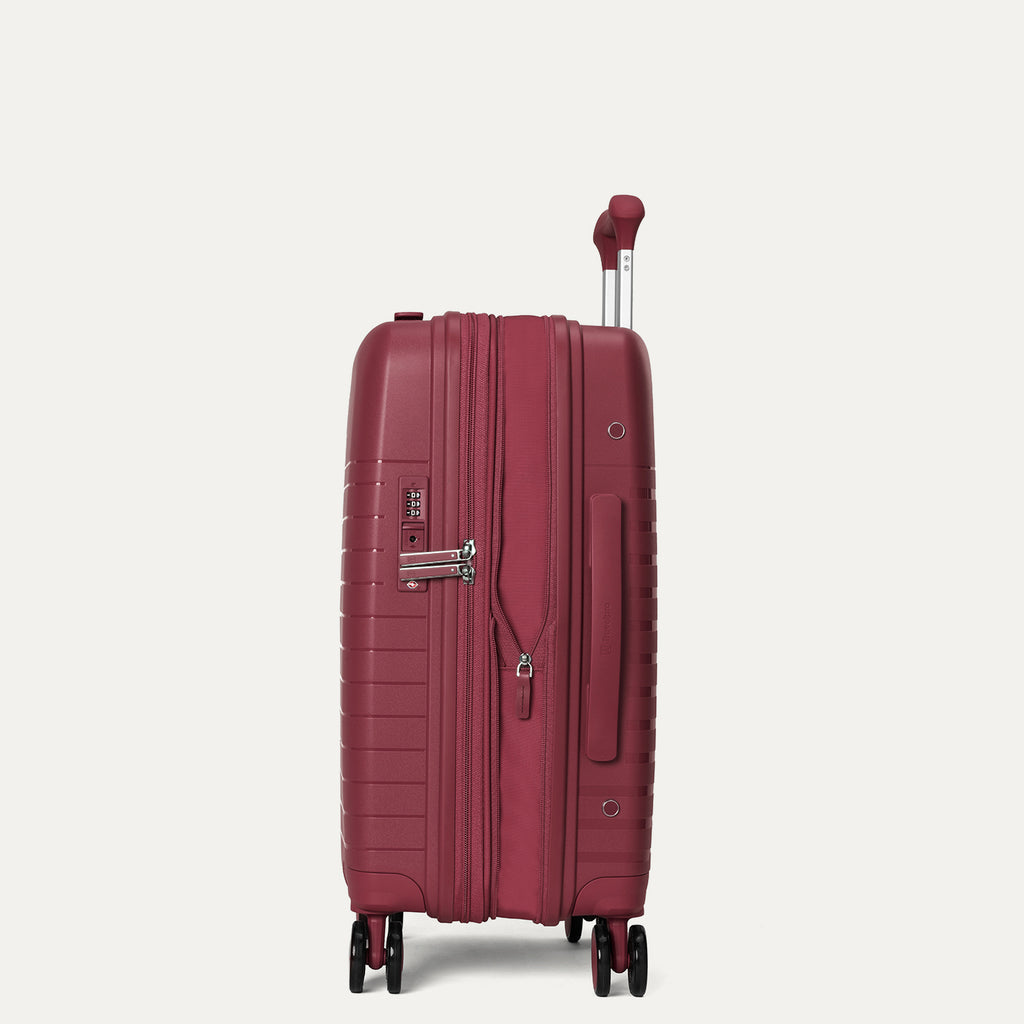 side profile view of the tibetan red travelpro optima® expandable carry-on hardside spinner, shown with the zippered expansion feature fully open to provide additional packing capacity.
