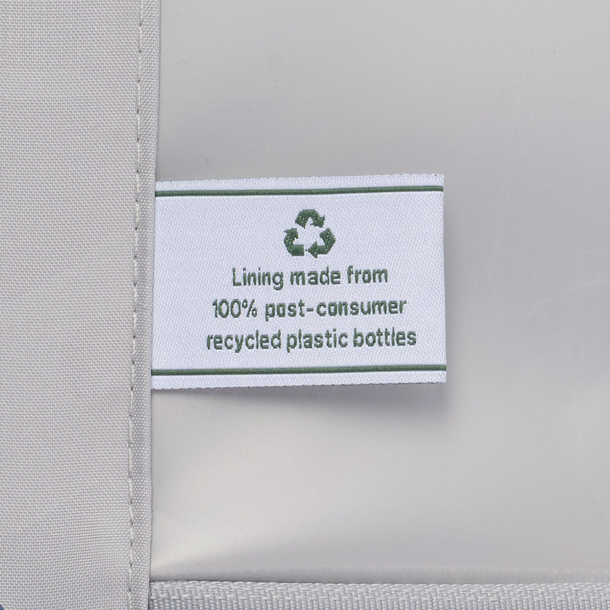 close-up view of the interior lining of the tibetan red travelpro optima® hardside carry-on, showing a white fabric label with a green recycling symbol that reads , lining made from 100% post-consumer recycled plastic bottles.