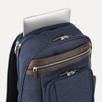 close-up view of the true navy travelpro platinum elite business laptop backpack 27l, showing a silver laptop being tucked into the dedicated padded electronics sleeve with dark brown leather trim.