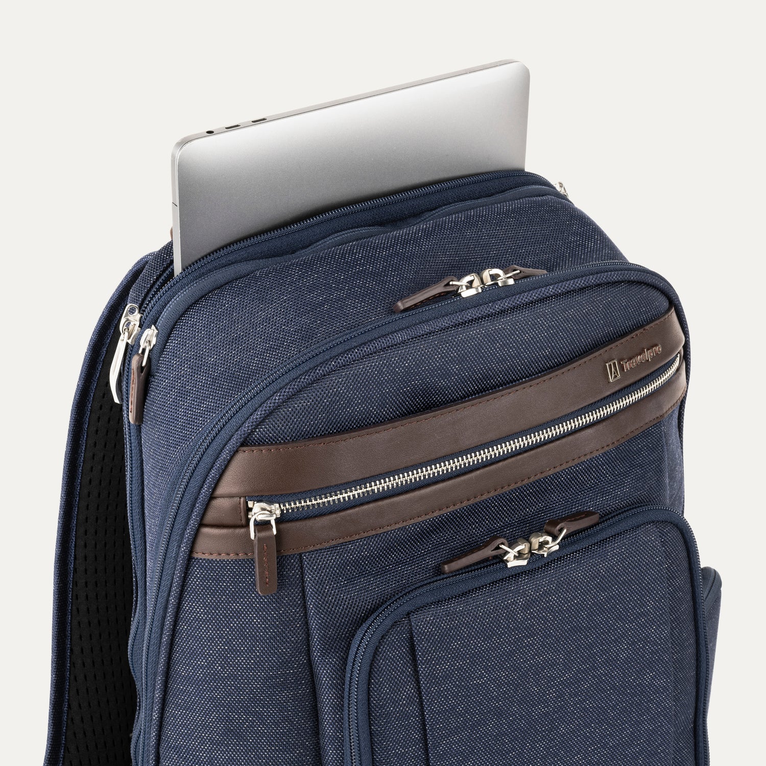 close-up view of the true navy travelpro platinum elite business laptop backpack 27l, showing a silver laptop being tucked into the dedicated padded electronics sleeve with dark brown leather trim.
