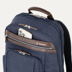 close-up view of the true navy travelpro platinum elite business laptop backpack 27l, showing a white smartphone being placed into the quickslip front pocket with magnetic closure and dark brown leather trim.