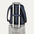 rear view of the true navy travelpro platinum elite business laptop backpack 27l stacked on a grey rolling suitcase, demonstrating the integrated trolley strap secured over the luggage handle.