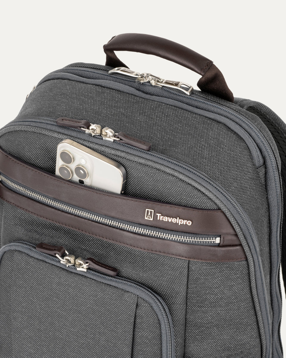 close-up view of the vintage grey travelpro platinum elite business laptop backpack 27l, showing a white smartphone being placed into the quickslip front pocket with magnetic closure and dark brown leather trim.