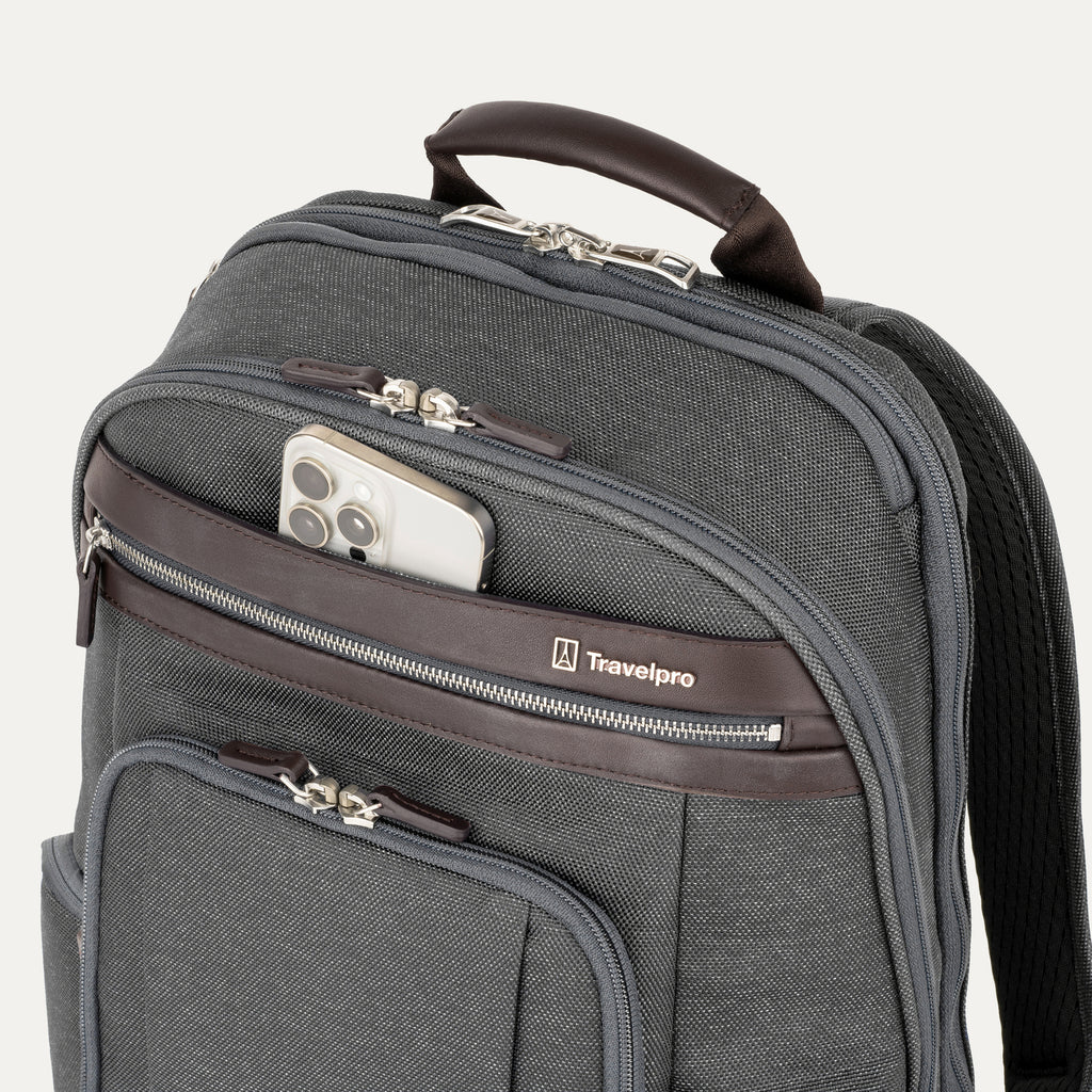 close-up view of the vintage grey travelpro platinum elite business laptop backpack 27l, showing a white smartphone being placed into the quickslip front pocket with magnetic closure and dark brown leather trim.
