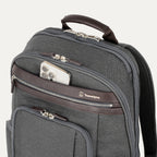 close-up view of the vintage grey travelpro platinum elite business laptop backpack 27l, showing a white smartphone being placed into the quickslip front pocket with magnetic closure and dark brown leather trim.