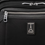 close-up view of the shadow black travelpro platinum® elite carry-on spinner tote, showing the chrome zipper pulls with the travelpro logo, a leather-trimmed pocket edge, and the metal travelpro logo badge on the front panel.