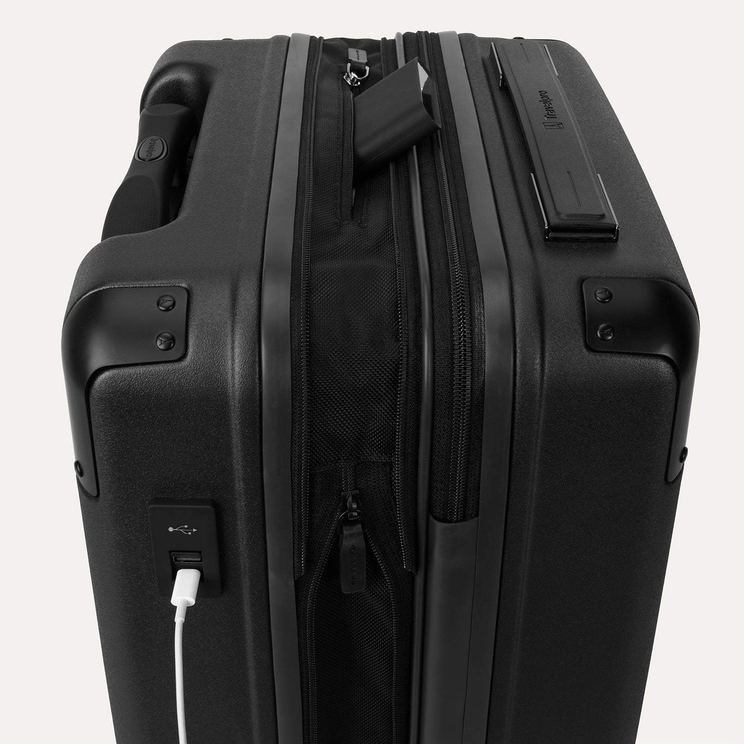 Close-up of the external charging ports on the Travelpro Platinum Elite Compact Carry-On Hardside Spinner in Shadow Black, showing a white cable plugged into the USB port and a power bank tucked into the dedicated battery sleeve within the expansion gusset.