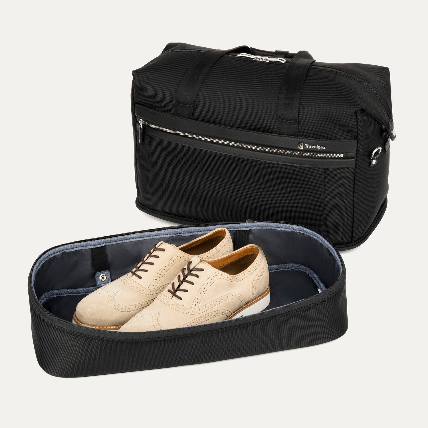 a view of the black travelpro platinum elite drop-bottom weekender bag with the bottom section completely removed, showing a pair of tan wingtip shoes inside the detached compartment and the main bag sitting behind it.